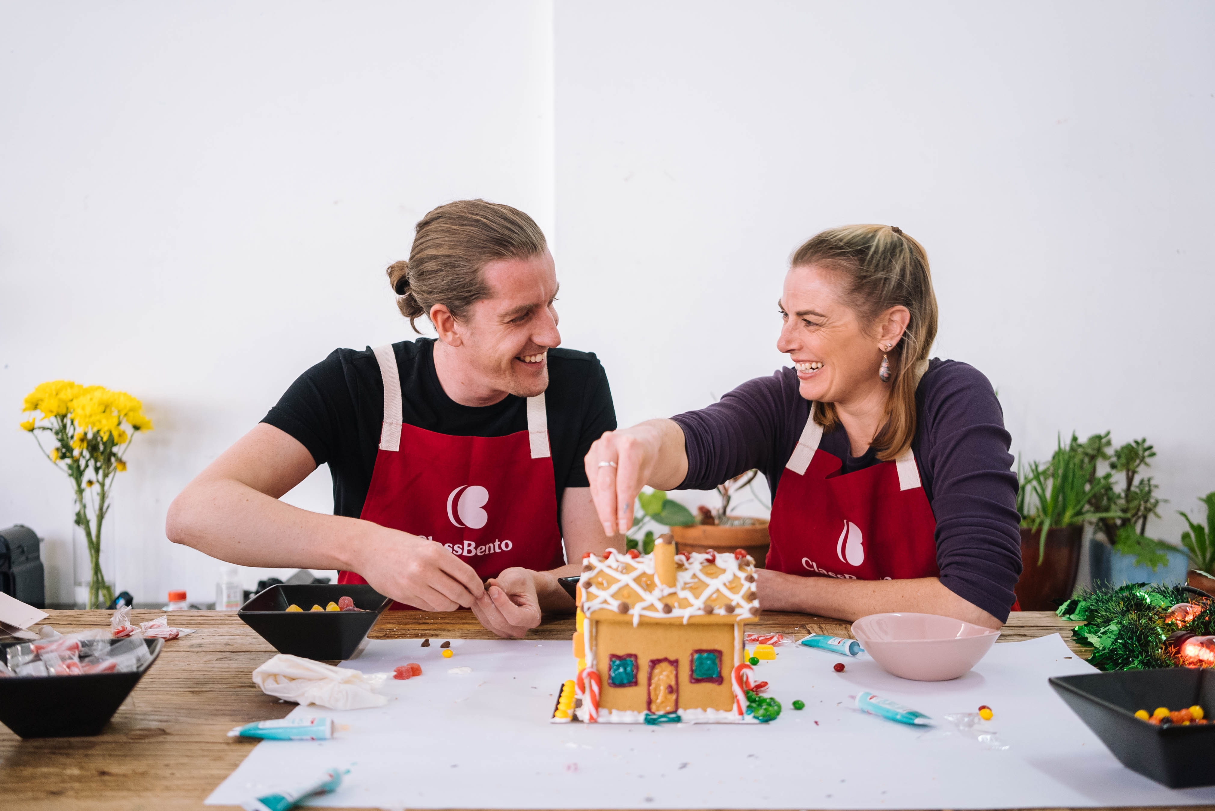 Smiling people decorating a gingerbread house in a Christmas baking workshop